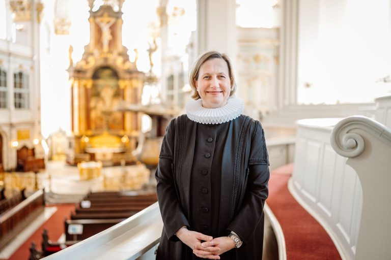 Pastorin Corinna Senf im Talar in der Kirche. Im Hintergrund ist der Altar zu sehen.