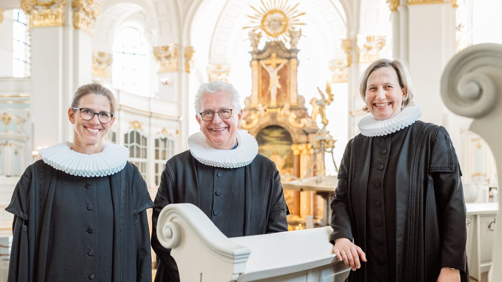 Pastorin Julia Atze, Hauptpastor Alexander Röder und Pastorin Corinna Senf stehen im Talar auf der Empore des Michel, Im Hintergrund ist der Altarraum zu sehen