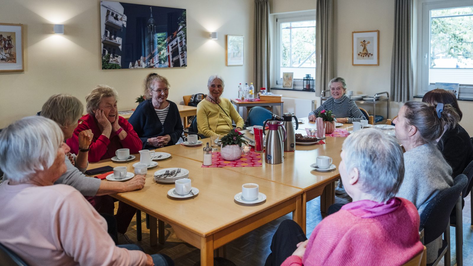 Frauen des Michel-Treffs sitzen am mit Kaffee und Kuchen gedeckten Tisch und unterhalten sich.