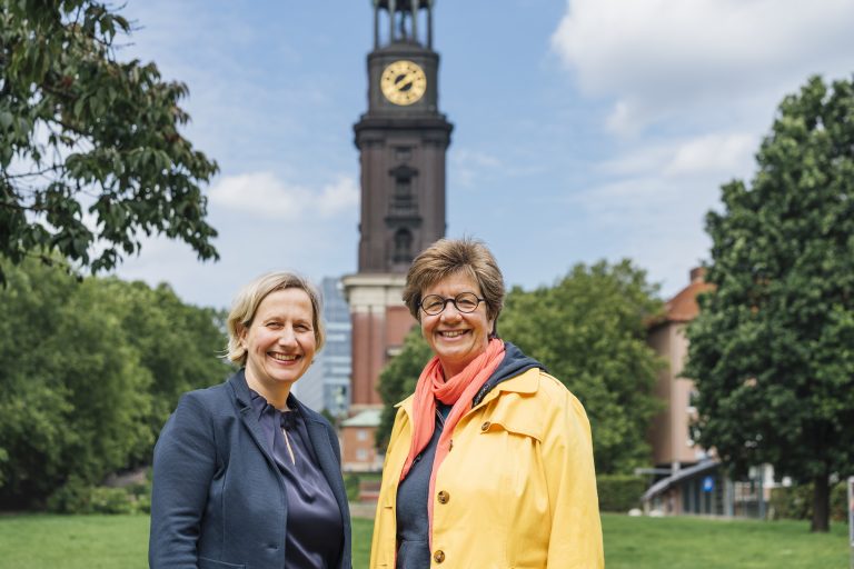 Pastorin Corinna Senf und Diakonin Anke Frickmann auf der Michel-Wiese. Im Hintergrund ist der Michel zu sehen.