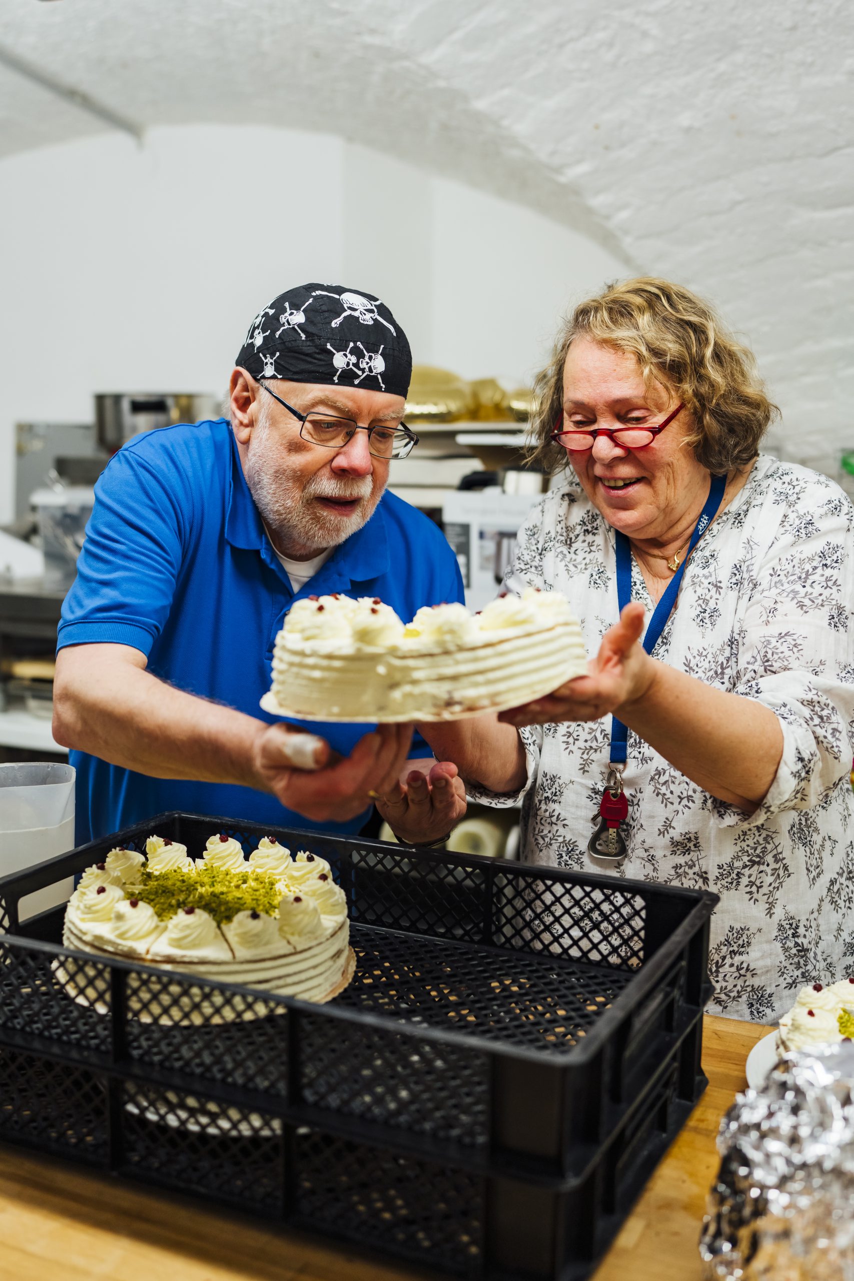 Zwei Ehrenamtliche heben eine Torte aus einem Korb.
