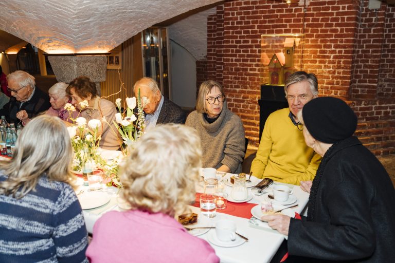 Die Stifter sitzen um den festlich geschmückten Tisch in der Krypta und genießen die Kuchen.
